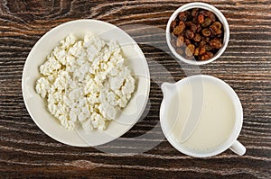 Plate with cottage cheese, bowl with raisin, pitcher with yogurt on wooden table. Top view