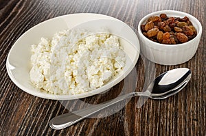 Plate with cottage cheese, bowl with raisin, spoon on wooden table