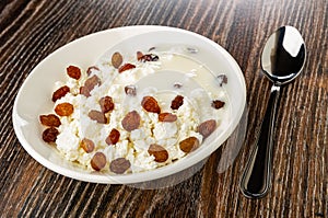 Plate with cottage cheese and raisin poured yogurt, spoon on wooden table