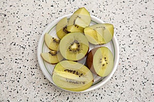 Plate of cut fresh kiwis on white table with pattern, top view