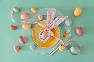 Plate decorated bunny ear napkin, white tulips and Easter eggs on blue background. Easter celebration concept. Flat lay. Top view