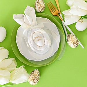 Plate decorated bunny ear napkin, white tulips and Easter eggs on green background. Easter celebration concept. Flat lay. Top view