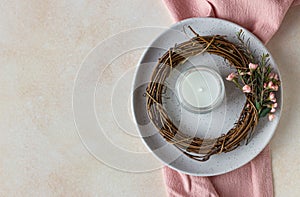 Plate with decorative spring wreath made of twigs and flowers and a candle, light concrete background. Romantic, wedding or spring