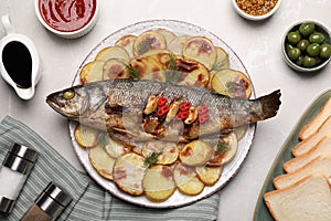 Plate with delicious baked sea bass fish and potatoes on light grey table, flat lay