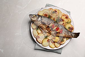 Plate with delicious baked sea bass fish and potatoes on light grey table, top view. Space for text