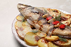 Plate with delicious baked sea bass fish and potatoes on light table, closeup