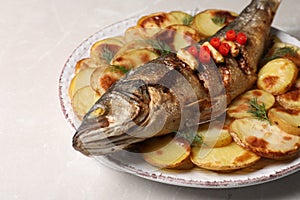 Plate with delicious baked sea bass fish and potatoes on light table, closeup