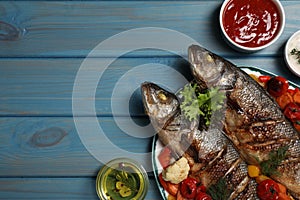 Plate with delicious baked sea bass fish and vegetables on light blue table, flat lay. Space for text