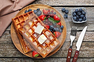 Plate of delicious Belgian waffles with honey, berries and butter on wooden table, flat lay