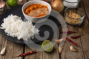 Plate with delicious chicken tikka masala curry and rice on rustic wooden table with spices background. Traditional Indian dish.