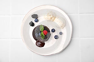 Plate with delicious chocolate fondant, berries, ice cream and mint on white tiled table, top view