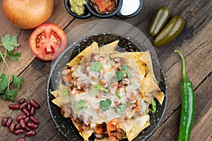 A plate of delicious corn chips nachos in cheddar cheese with beans, tomato, green chili, black olives, cilantro served with guaca