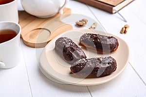 Plate with delicious eclairs and cup of tea on white wooden table