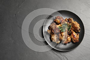 Plate with delicious fried chicken wings on black table, top view. Space for text