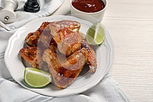 Plate with delicious fried chicken wings and lime on white wooden table
