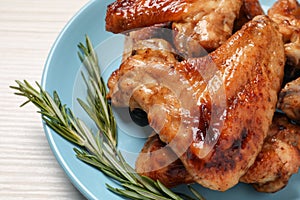 Plate with delicious fried chicken wings and sprig of rosemary on white wooden table, closeup