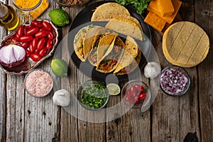 Plate with delicious mexican tacos on rustic wooden table with ingredients for cooking background. Concept of traditional meal.