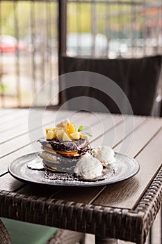 Plate of delicious pancakes with chocolate and fruits served with two balls of ice cream