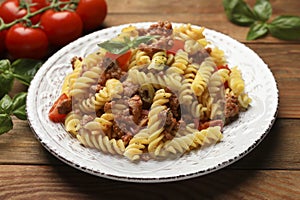 Plate of delicious pasta with minced meat, tomatoes and basil on wooden table, closeup