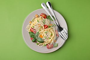 Plate of delicious pasta primavera and cutlery on light green background, top view