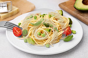 Plate of delicious pasta primavera and ingredients on light gray table, closeup
