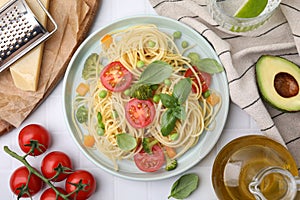 Plate of delicious pasta primavera and ingredients on white table, flat lay