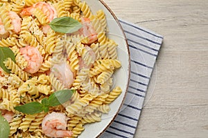 Plate of delicious pasta with shrimps, basil and parmesan cheese on light wooden table, top view. Space for text