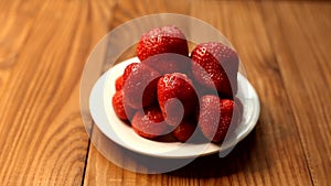 A plate of delicious ripe strawberries. Fresh strawberries in a white plate illuminated by light with shadows around.