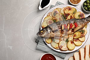 Plate with delicious roasted sea bass fish and potatoes on light grey table, flat lay. Space for text