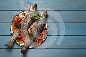 Plate with delicious roasted sea bass fish and vegetables on light blue table, top view