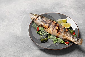 Plate with delicious sea bass fish and ingredients on light grey table, space for text