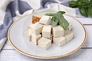 Plate with delicious smoked tofu and basil on white wooden table, closeup