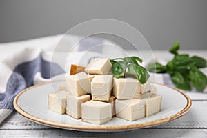 Plate with delicious smoked tofu and basil on white wooden table, closeup