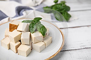 Plate with delicious smoked tofu and basil on white wooden table, closeup