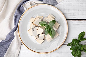 Plate with delicious smoked tofu and basil on white wooden table, top view