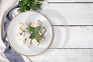 Plate with delicious smoked tofu and basil on white wooden table, top view. Space for text