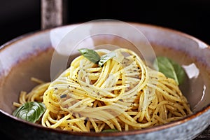 Plate of delicious spaghetti pesto garnished with parmesan cheese and basil on rustic dark background