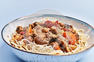 Plate of delicious spaghettis with meat and vegetables over blue background