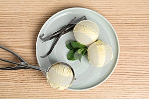 Plate with delicious vanilla ice cream, mint, pods and scoop on wooden table