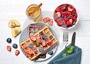 Plate with delicious waffles, berries and honey on white wooden table