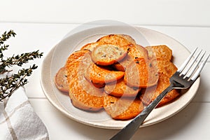 Plate with deliciously cooked sweet potatoes, rosemary, sauce and spices, herbs on a wooden