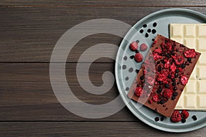 Plate and different chocolate bars with freeze dried fruits on wooden table, top view. Space for text