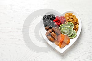 Plate of different dried fruits on wooden background, top view with space for text