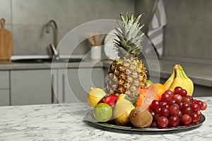 Plate with different ripe fruits on white marble table in kitchen. Space for text