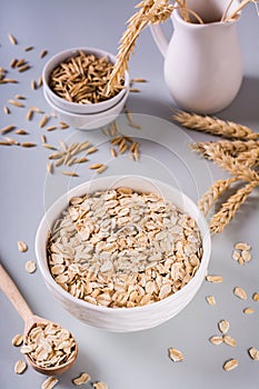 A plate with dry oatmeal and ears of oats on a gray background. Vertical view