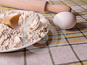 Plate of flour, eggs and a wooden rolling pin on the table.