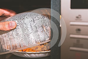 Plate with food warmed in the microwave. The question of the benefits and dangers of radiation microwaves for food. Cook opens the