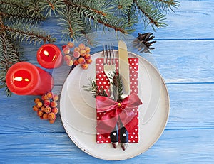 Plate, fork, knife, branch of a Christmas tree, bow on a blue wooden background, candle photo