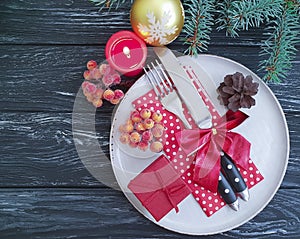 Plate, fork, knife, candle, bump celebration serving branch menu of a Christmas tree on a dark wooden background