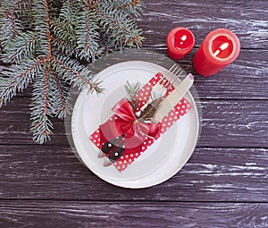 Plate, fork, knife, candle, dining celebration serving branch menu of a Christmas tree on a dark wooden background